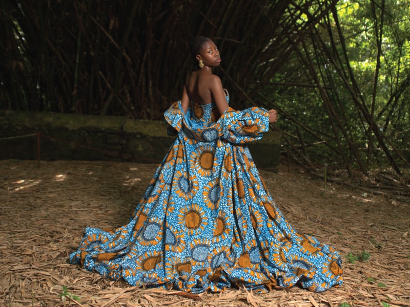 An African woman poses in a forest in a blue printed gown