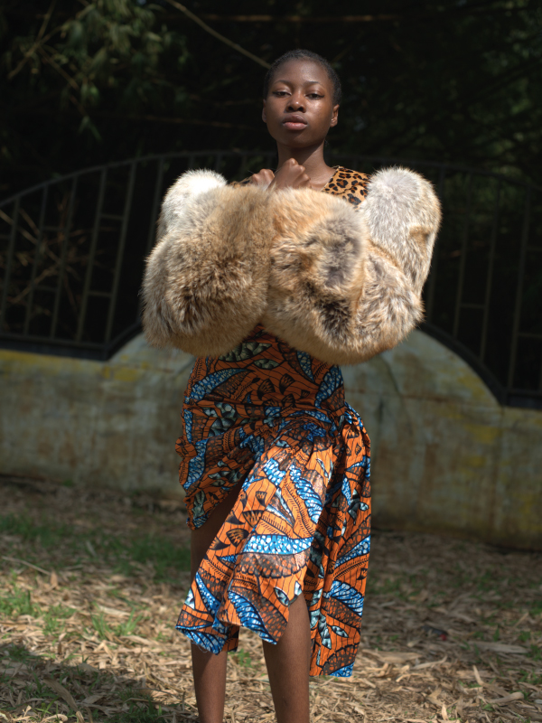 An African woman poses in a colourful blue and orange dress and fur coat
