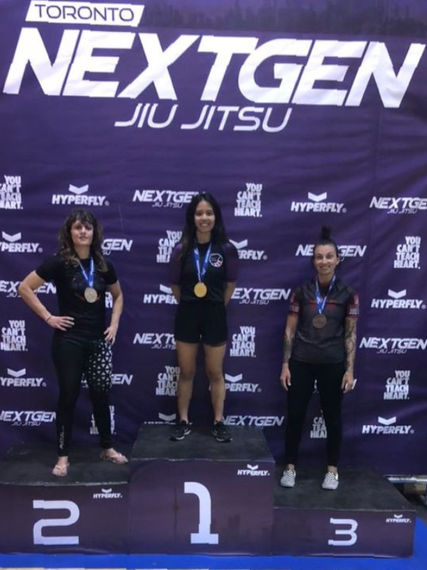 three women standing on a poduim weraing their repsective medals 