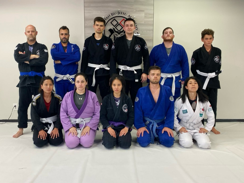 A group of men and women wearing  jiu jitsu gis lined up and posing for a picture 