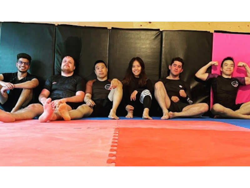 A group of men and women sitting down on mats wearing rash guards 