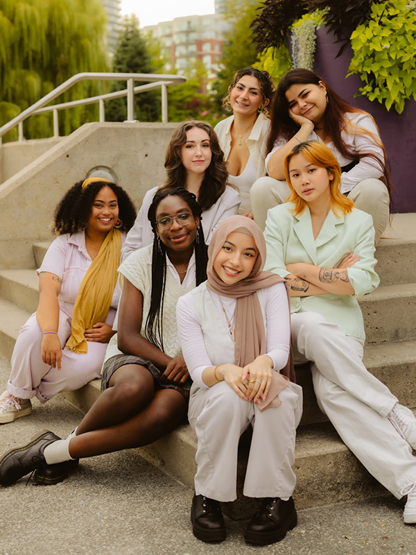 Six executive members of Rebelle Zine sit on stairs and smile for the camera