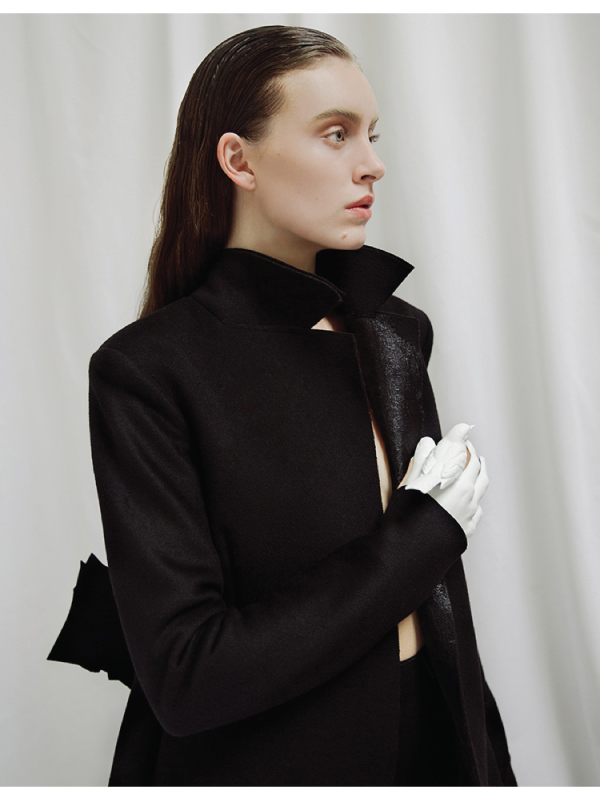 Woman with slick back hair and black jacket looks away from the camera