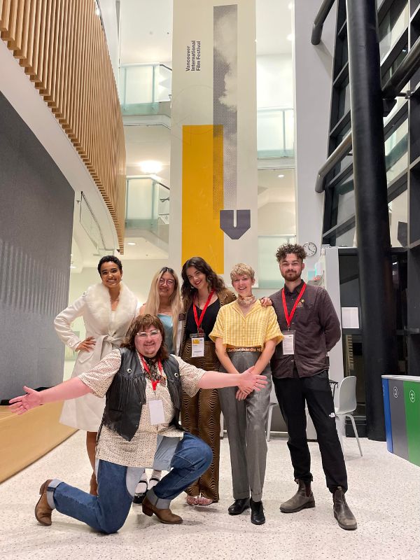 A group of people smile stand in a brightly lit hallway 