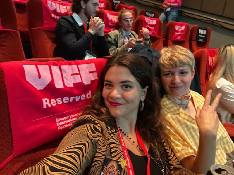 Two woman sitting in two reserved seats at a movie theatre 