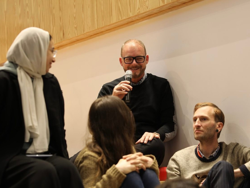 A man in the audience is smiling holding up a microphone surrounded by people 