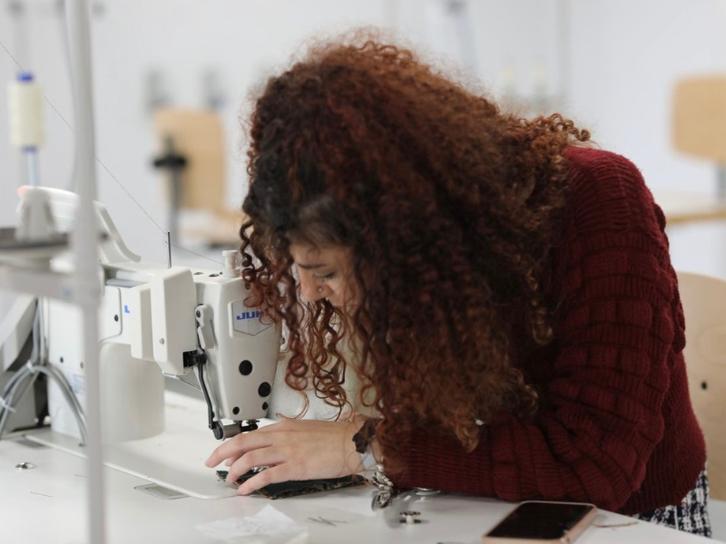 A woman with curly hair is using a sewing machine.
