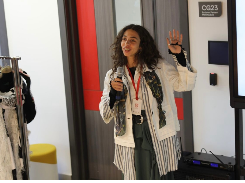 A woman is holding a microphone and presenting infornt of a slide deck 