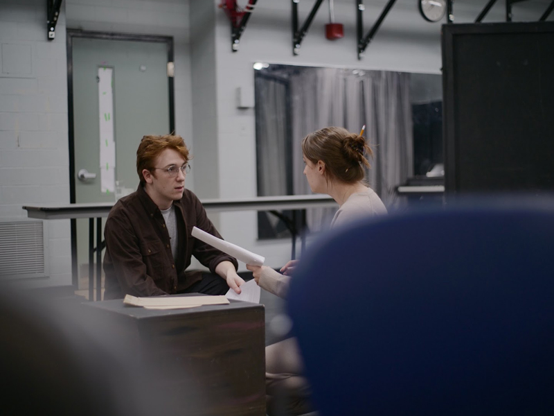 Students sit across from one another acting during a scene with scripts in hand
