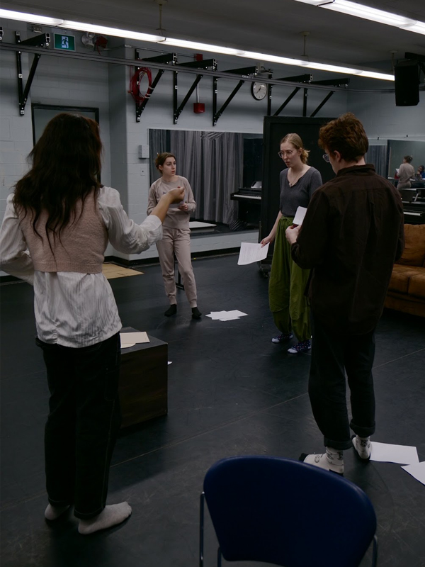 Students stand dramatically acting during their rehearsal