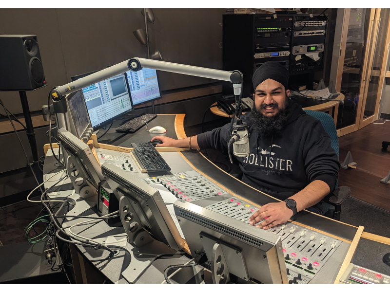 Kuwarjeet in front of a soundboard and a microphone for CBC radio
