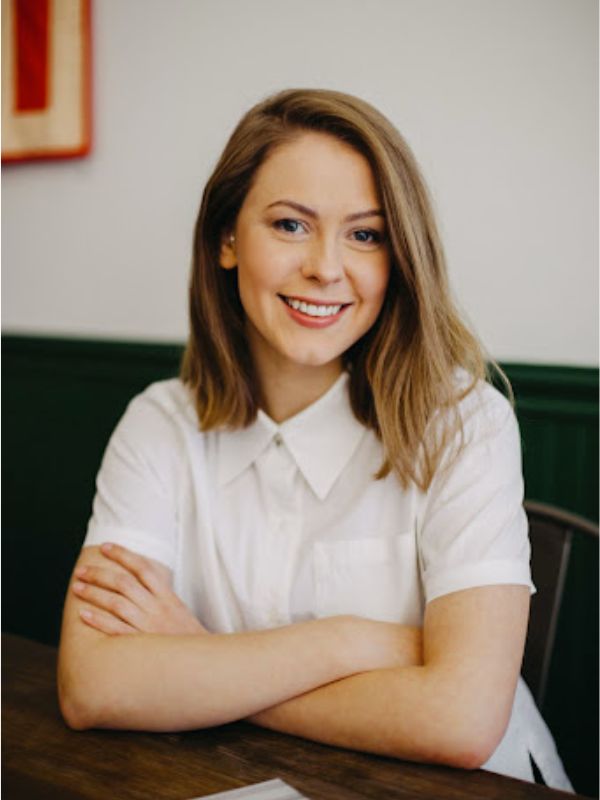 A woman standing with her arms crossed and enthusiastically smiling. 