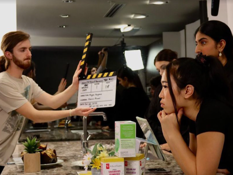 A man holds a a clapper in front of three actors getting ready for a scene.
