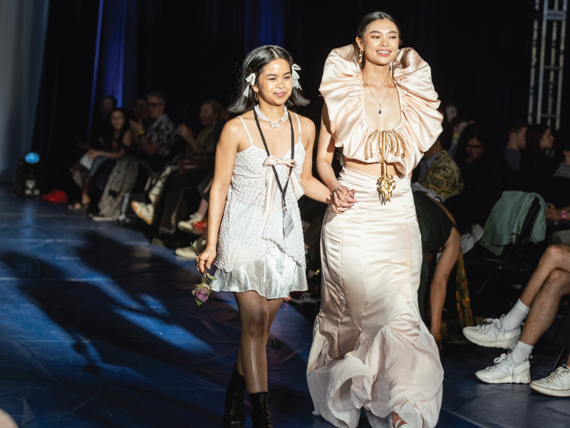 Two women hold hands in their all white outfits down the runway