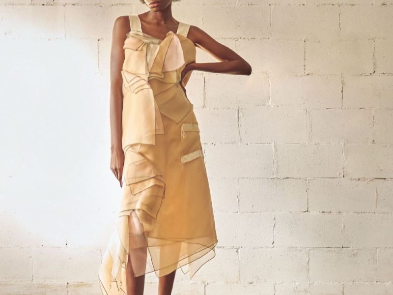 A yellow dress garment on a model in front of a white brick background