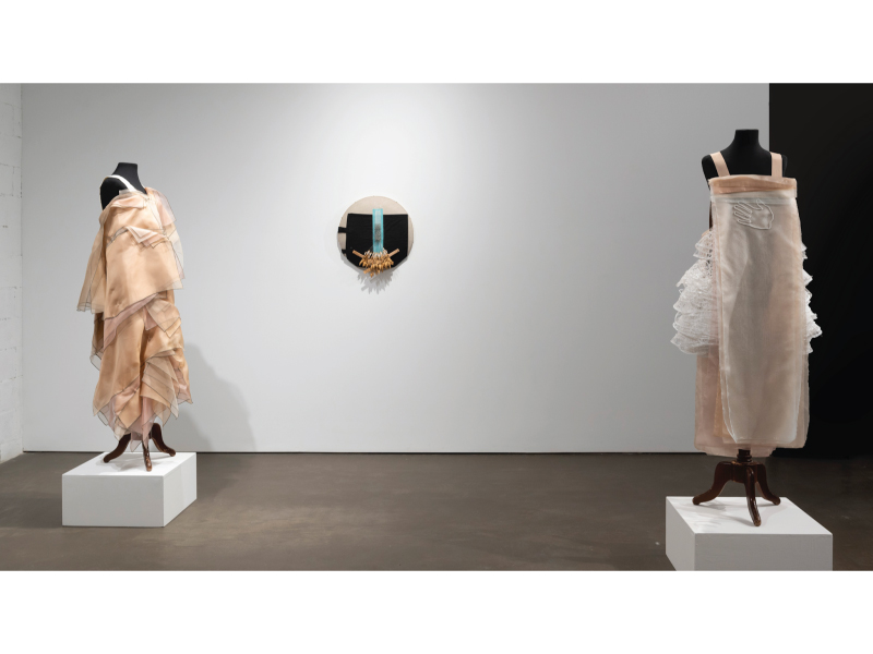 Two garments on mannequinns in a gallery on block pedestals in front of a white wall