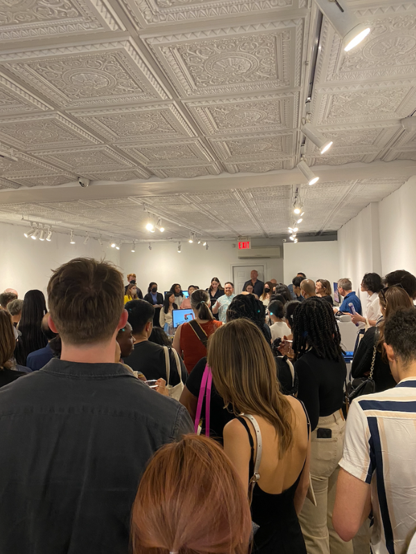 A gallery space is packed with attendees all facing a speaker as they give opening remarks.