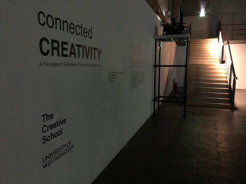 A wall with vinyl text that reads "Entry way to the Connected Creativity: A Transatlantic Exhibition of Practice-Based Research," "The Creative School," and "University of Westminister. 
