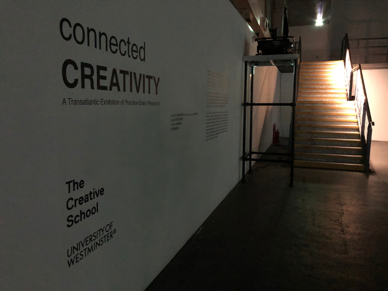 A wall with vinyl text that reads "Entry way to the Connected Creativity: A Transatlantic Exhibition of Practice-Based Research," "The Creative School," and "University of Westminister.
