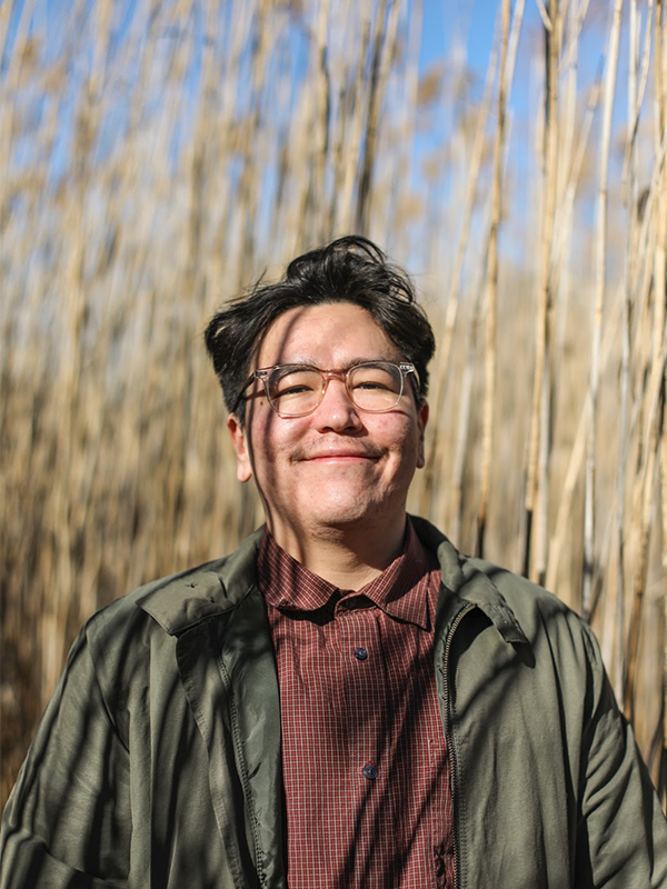 Portait of Media and Design Innovation PhD student Fallon Simard in a brick red shirt, green jacket and clear glasses