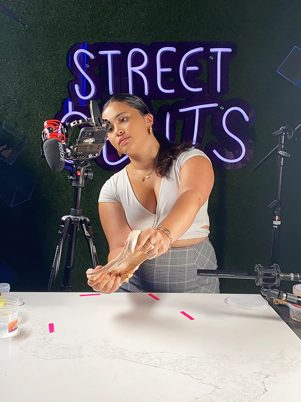 Street Cents co-host in the studio playing with slime and creating content using a tri-pod