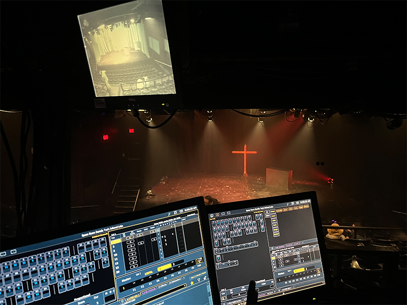 Production control screens and panels that view the main stage theatre where a large cross.is placed.  
