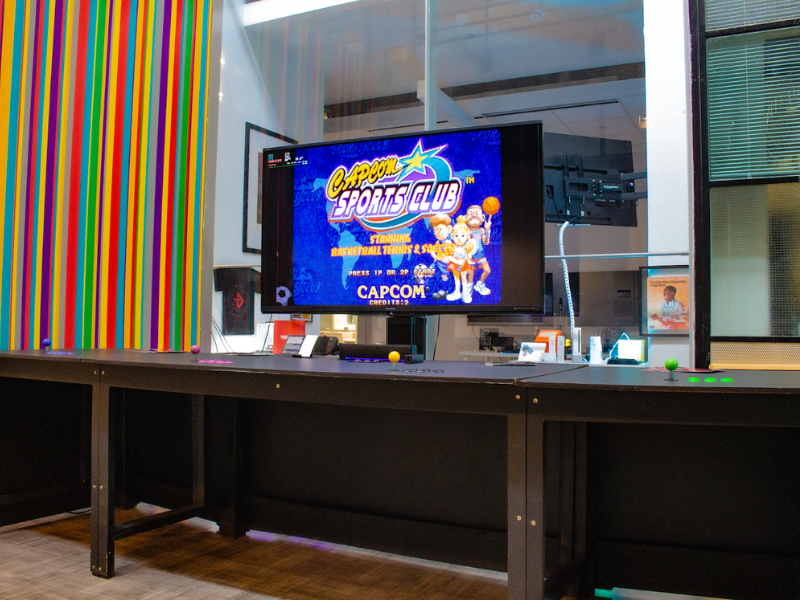 An arcade table with a television is prominently displayed in a brightly lit hallway