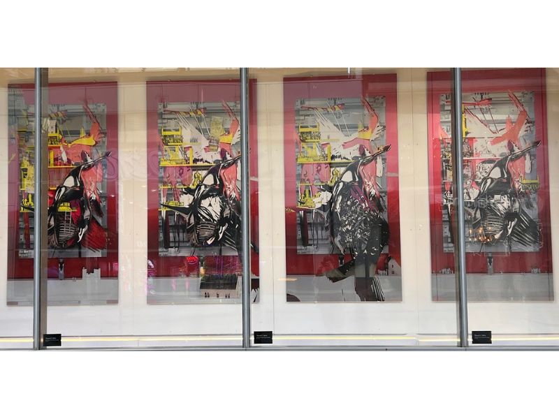 Window display showing faculty artwork. The artwork is abstract with a black whale as the main subject surrounded by colours of red, white, and yellow. 
