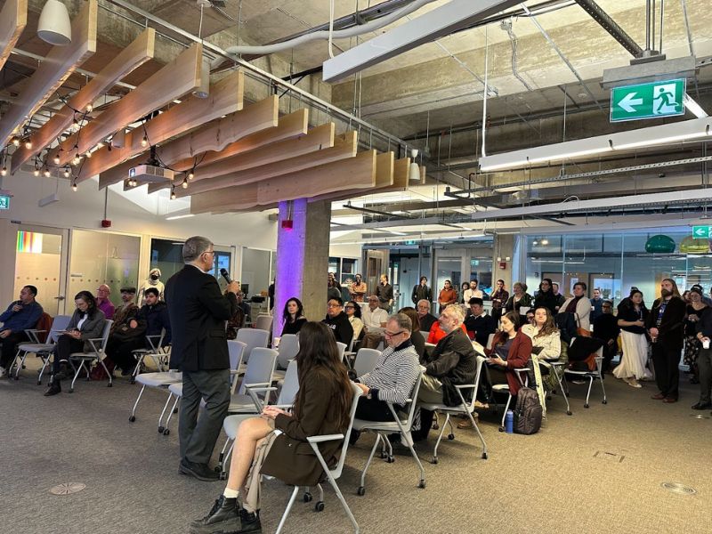 Dean Charles Falzon stands and delivers a speech into a microphone in front of the seated audience.