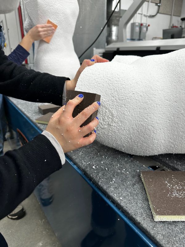 A hand uses sandpaper to smooth the white foam carved forms