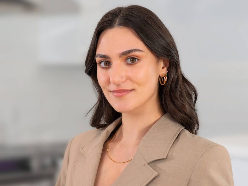 A woman wearing a beige blazer and gold accessories poses for a photo shoot
