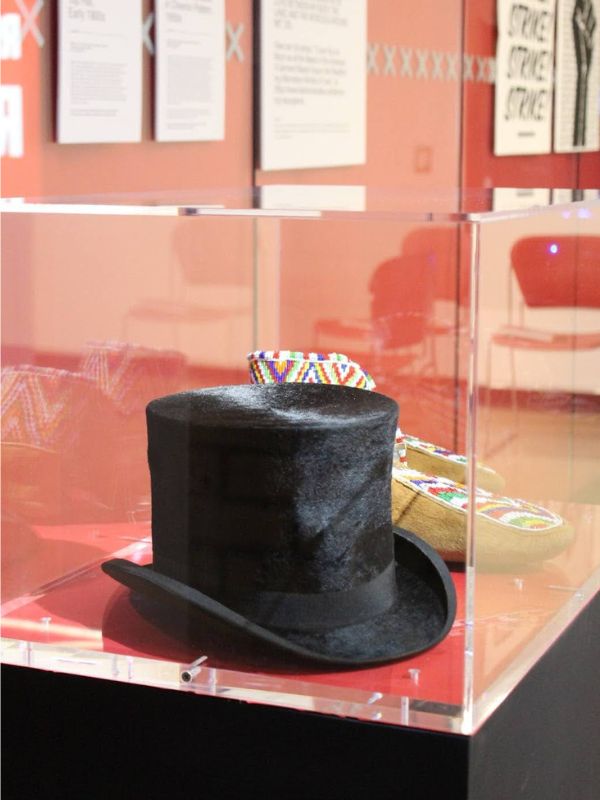 A glass showcase displaying a rabbit fur felt hat and Cree moccasins beaded in chevron pattern