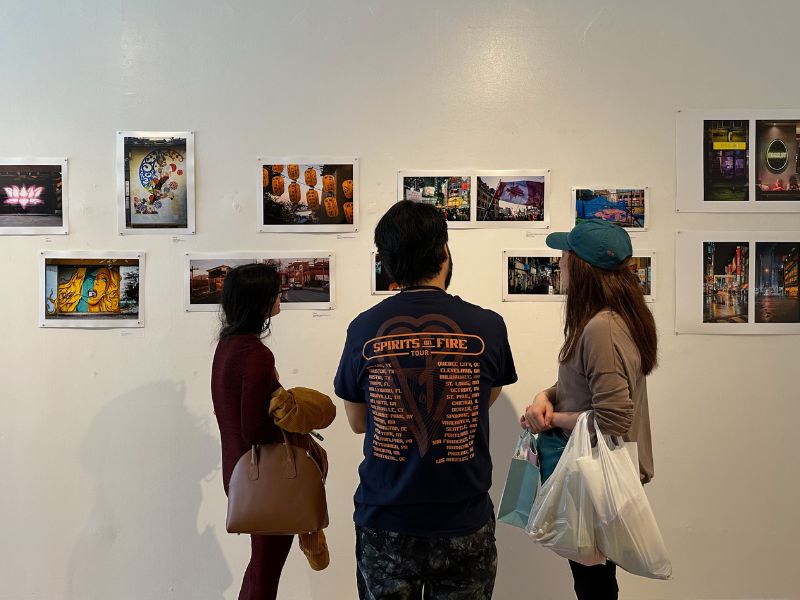 Two women and a man (artist) observe a wall of photography with their backs turned to the camera.