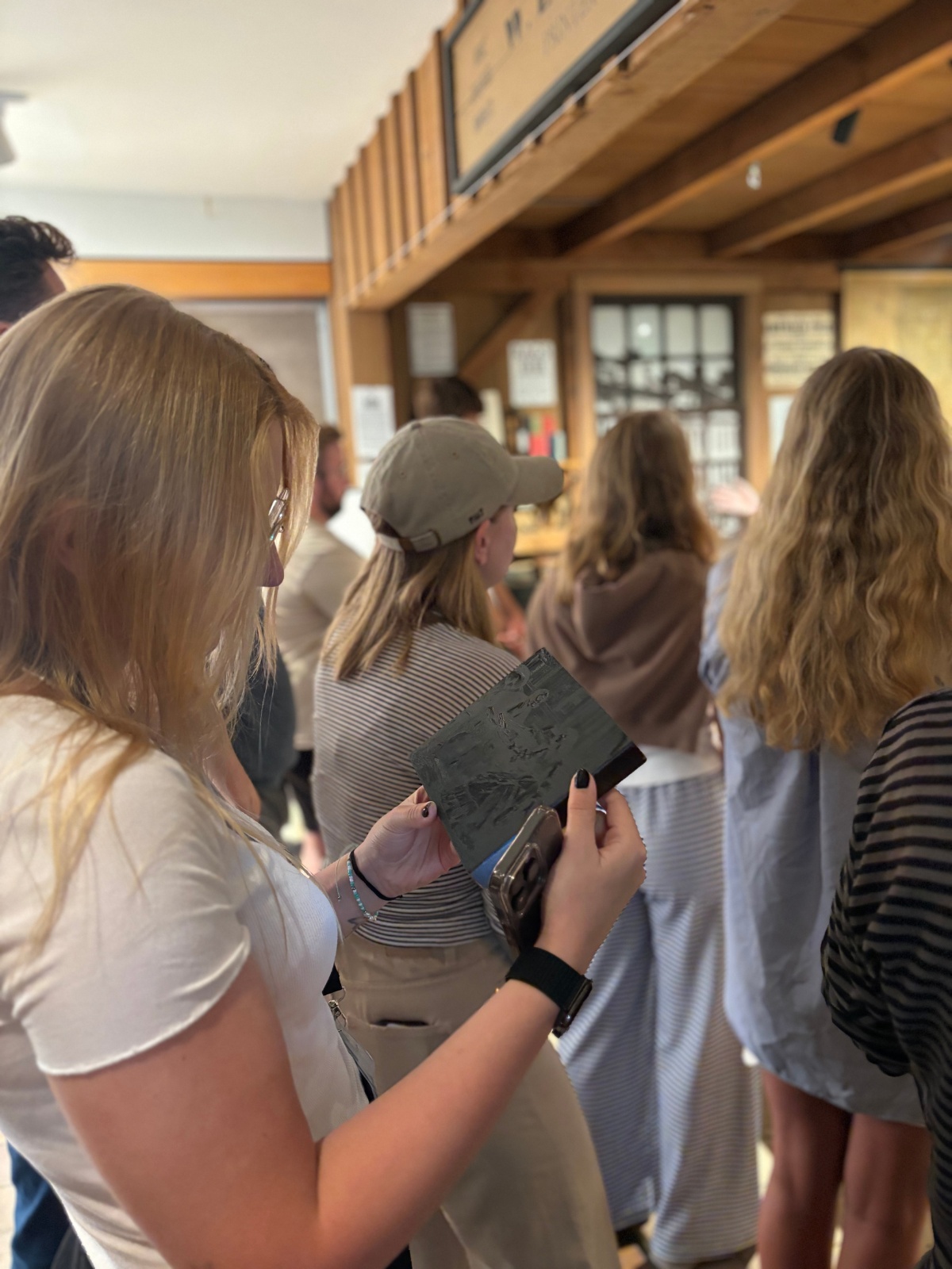Medium shot of a woman observing a woodblock print while other trainees are scattered around her. 