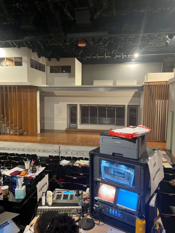 A theatre room with computer equipment buzzing to life in the foreground and an empty stage in the background.