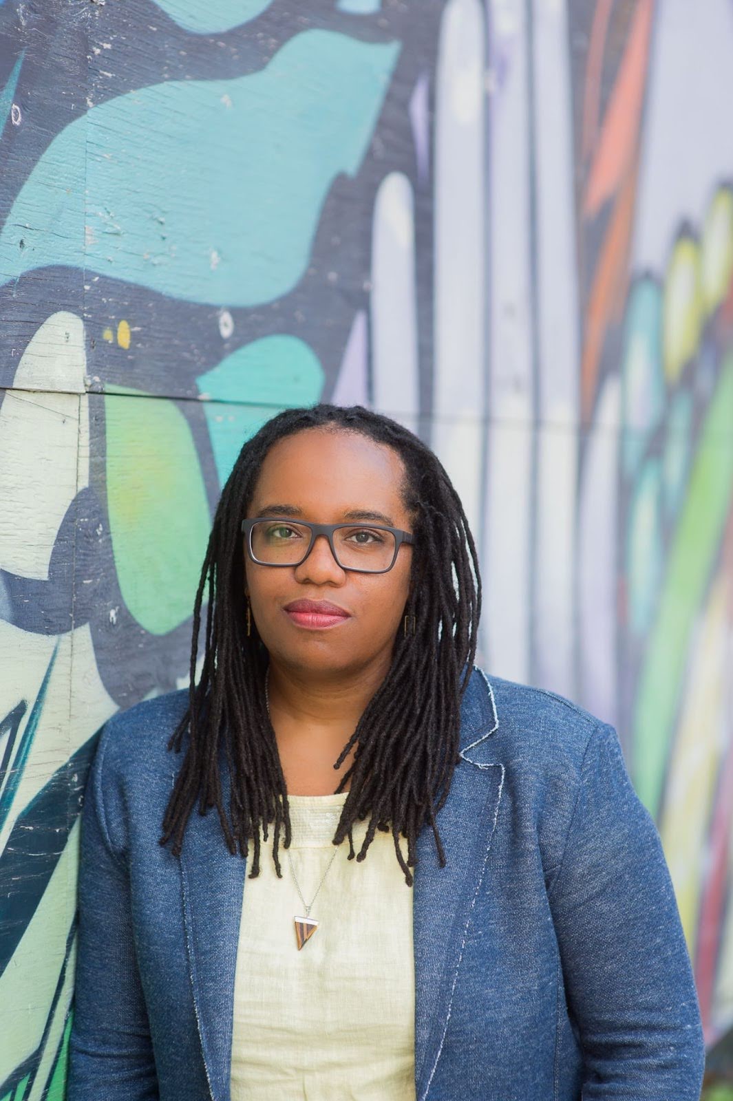Woman posed against a graffiti wall and wearing a yellow shirt and blue blazer