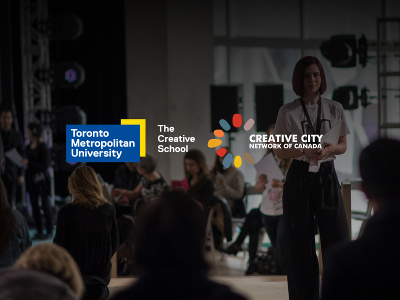 An image of a woman wearing a badge in a venue, with an audience seated in chairs surrounding her. Overlaid are the TMU and The Creative School logos, along with the Creative City Network of Canada logo.
