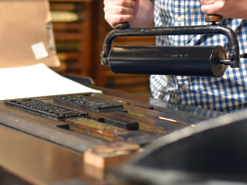 Close-up shot of a person holding an ink roller and inking up a letterpress.