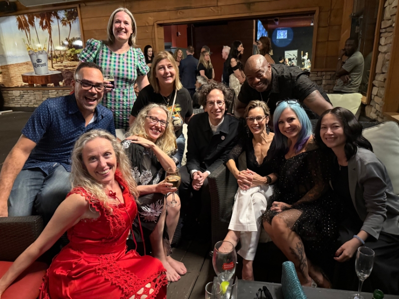 A group of eleven people gathers in an indoor setting while smiling and posing together on couches and chairs.