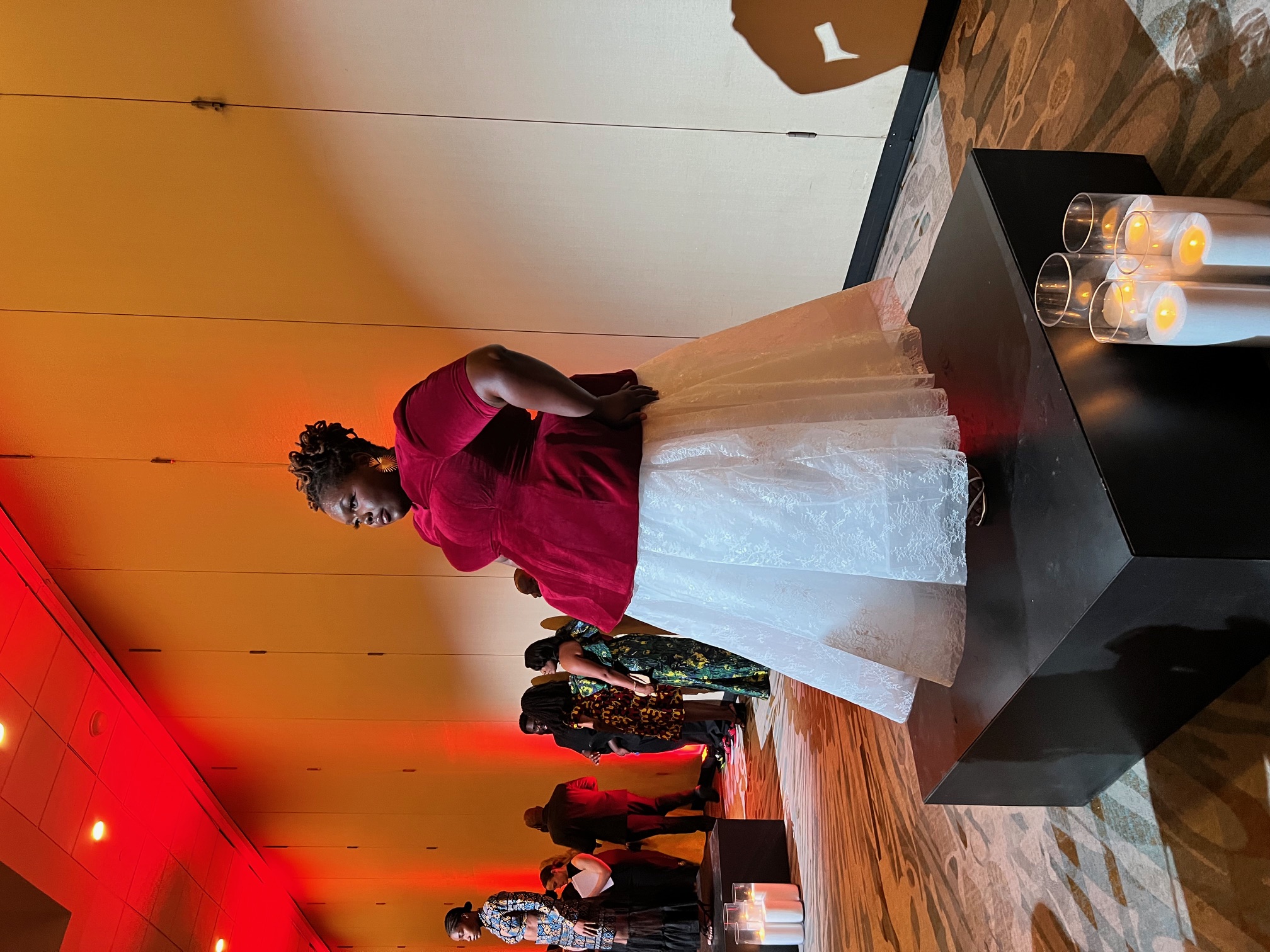 A model wears a red velvet top and white lace skirt during a fashion showcase lit in red tones.