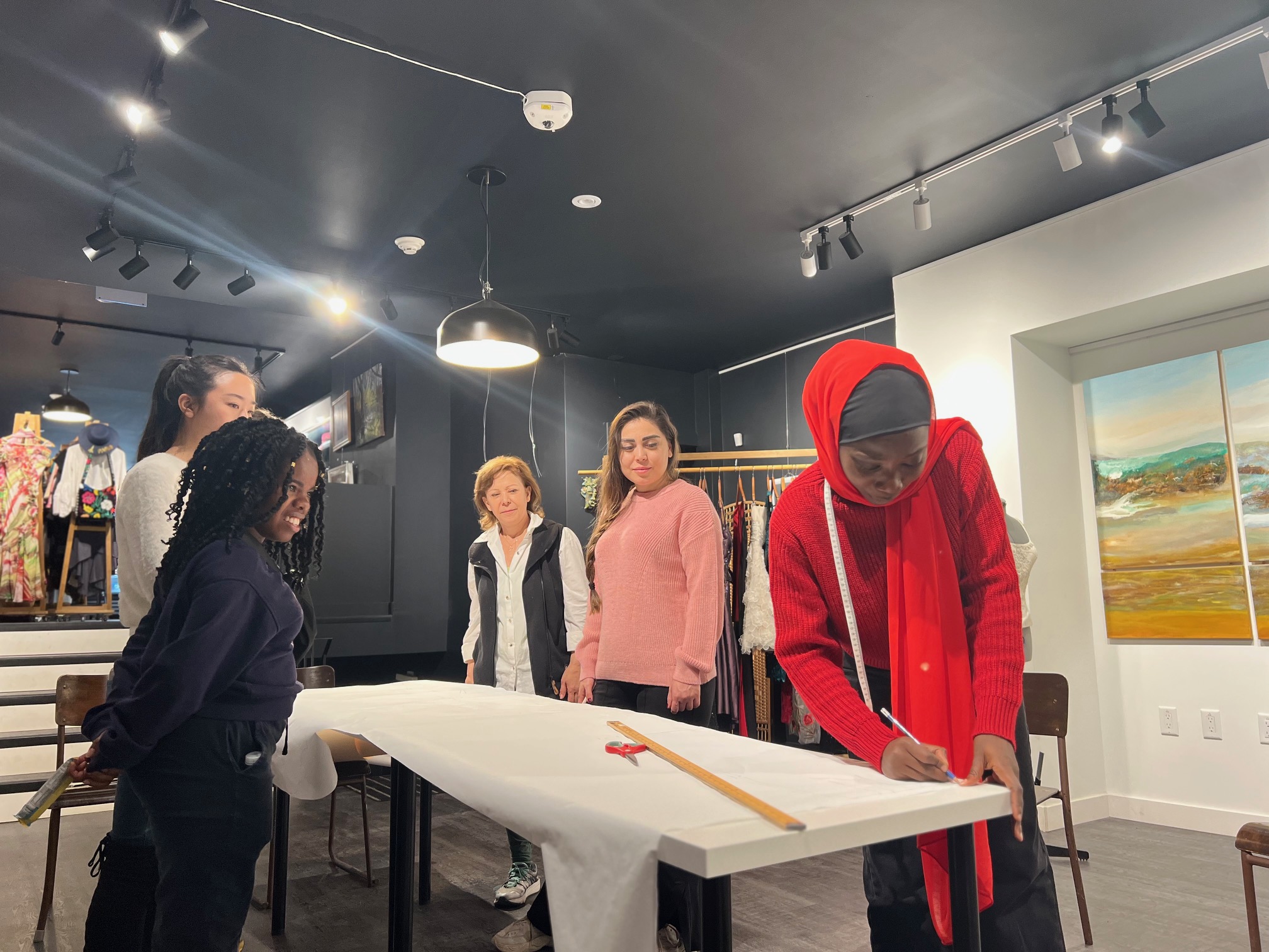 Azizah Adunola Alawusa, wearing a red scarf, measures fabric on a table with a small team of collaborators.