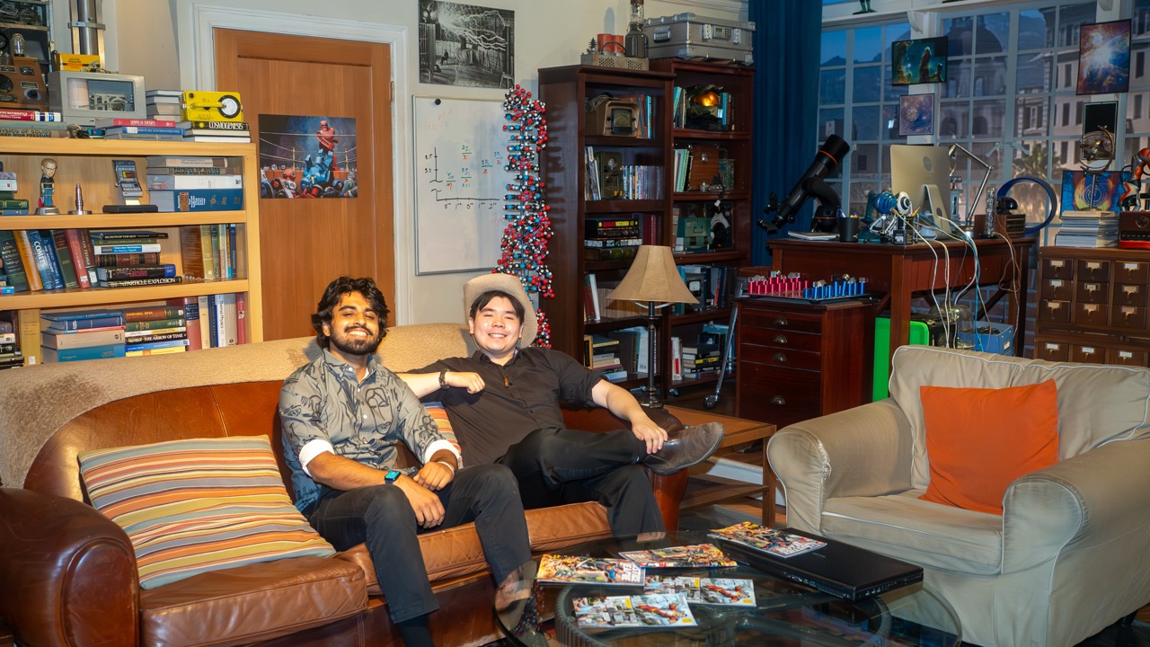 Two RTA in LA students in the apartment in“The Big Bang Theory”, sitting on a brown leather couch inside a studio space decorated with science props, bookshelves, and film memorabilia.