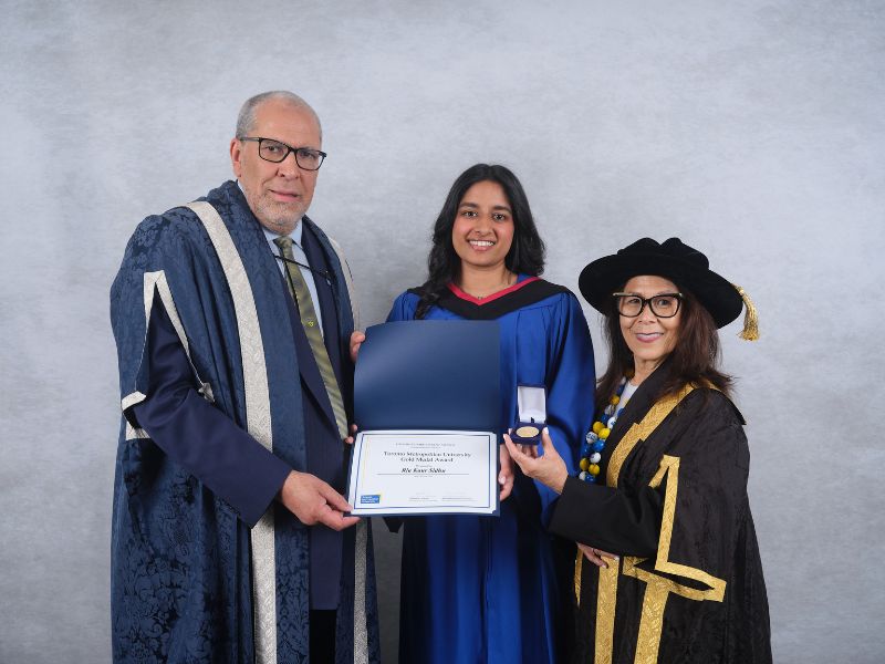 TMU President and Vice-Chancellor Mohamed Lachemi, Ria Sidhu and Chancellor Donette Chin-Loy Chang pose together during Convocation. Sidhu, wearing her blue graduation gown, holds her Gold Medal certificate while Chin-Loy Chang displays the Gold Medal.