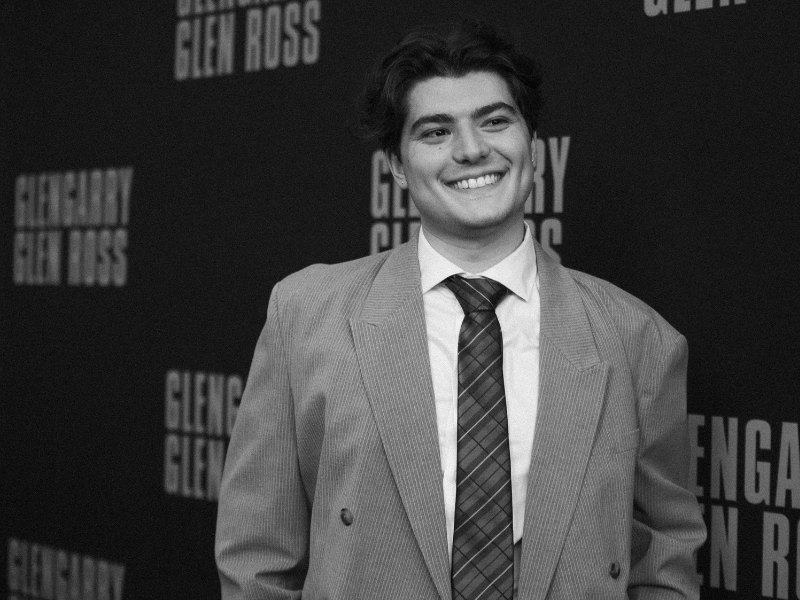 A smiling man in a suit poses in front of a "Glengarry Glen Ross" step-and-repeat backdrop.