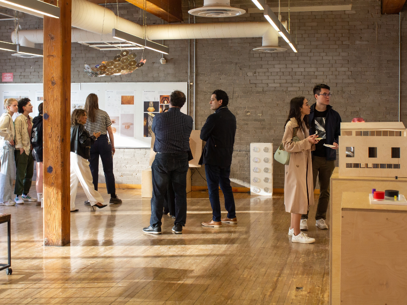 Exhibition attendees walk around building models and plans hung on the walls