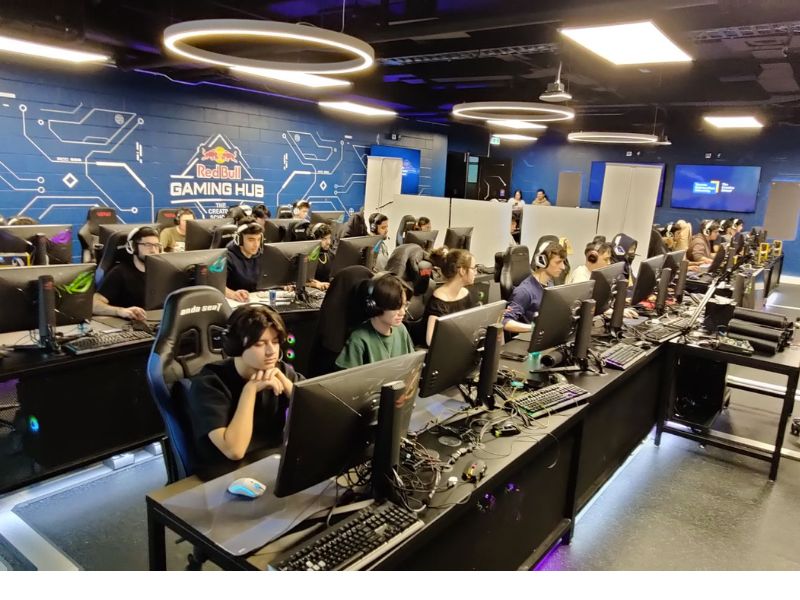 The Red Bull Gaming Hub mid-tournament. Students are shown wearing headsets and are seated at each PC. 