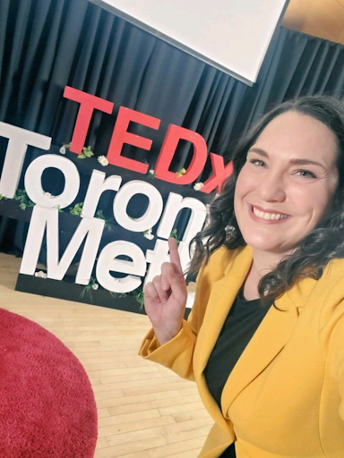 A woman wearing a vibrant yellow blazer takes a selfie on stage. 