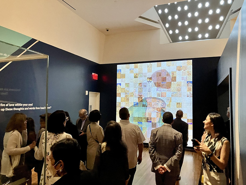 A crowd of people look at a large projection of Rumi’s portrait on a 10ft x 10ft wall that is made from a grid of hundreds of dynamically changing images