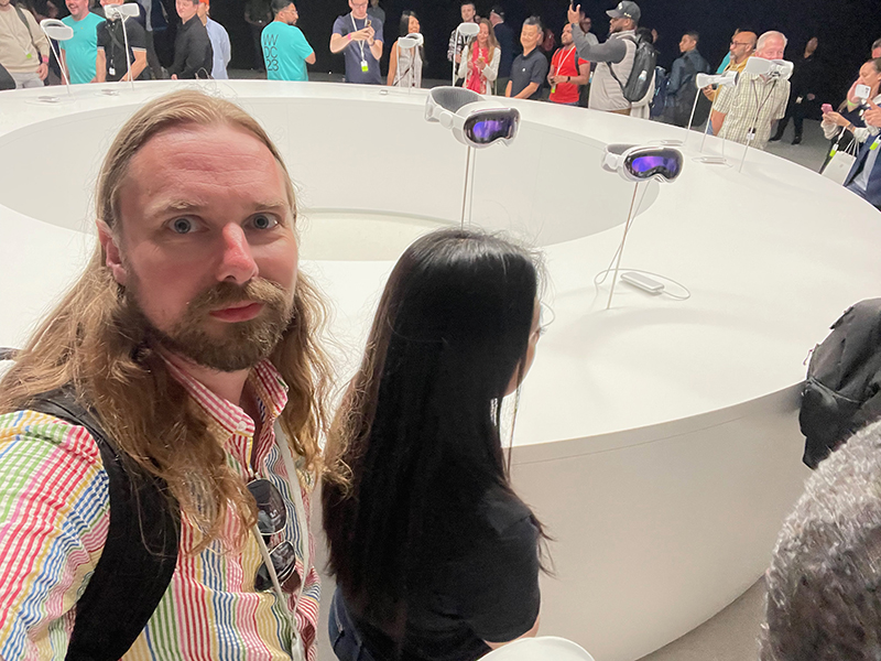 Professor Michael F. Bergmann is taking a selfie behind him is two VisionPro goggles mounted on stands.