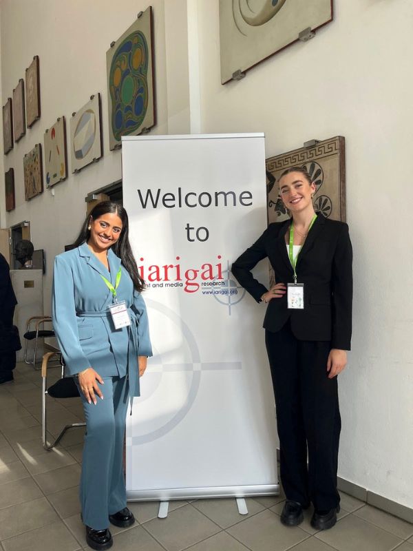 Two students taking a picture in front of a banner titled Welcome to IARIGAI